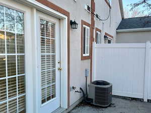 View of exterior entry with central air condition unit, a patio area, fence, and stucco siding