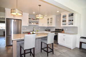 Kitchen featuring stainless steel appliances, composite sink, open shelves, tile flooring and tasteful backsplash