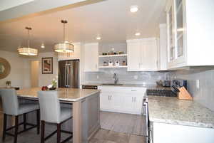 Kitchen featuring open shelves, backsplash, appliances with stainless steel finishes, white cabinetry, composite sink, gas stove