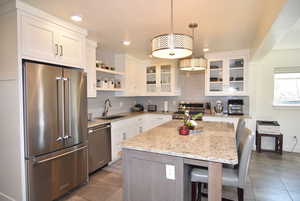 Kitchen featuring a breakfast bar area, stainless steel appliances, composite sink, open shelves, granite counter tops, tile floors and tasteful backsplash