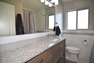 Full bathroom #2 featuring toilet, tile walls, granite countertops and a wealth of natural light.