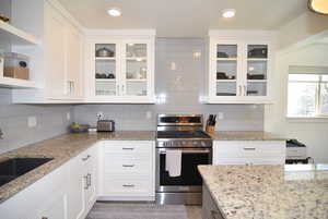 Kitchen featuring white cabinets, gas range, granite counters, open shelves, and a composite sink