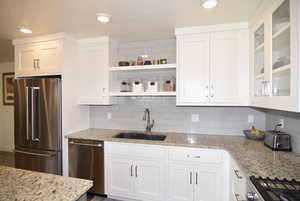 Kitchen with stainless steel appliances, backsplash, white cabinets.