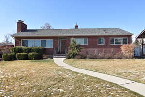 Ranch-style home featuring a shingled roof, a chimney, a front lawn, and brick siding