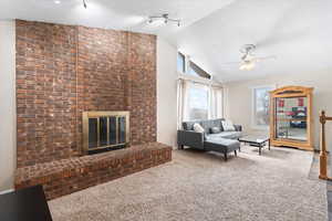 Carpeted living area featuring high vaulted ceiling, a brick fireplace, and ceiling fan