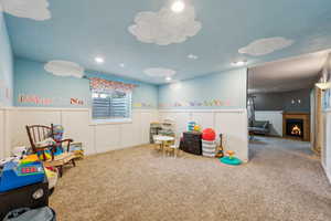 Playroom featuring carpet, a warm lit fireplace, and wainscoting