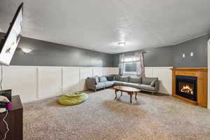 Living room with a textured ceiling, a glass covered fireplace, wainscoting, and carpet flooring