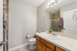 Full bathroom with tile patterned flooring, toilet, vanity, baseboards, and a stall shower