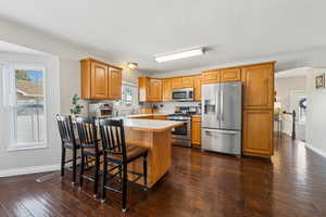 Kitchen featuring a peninsula, baseboards, light countertops, appliances with stainless steel finishes, and dark wood-style floors