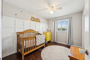 Bedroom with a nursery area, a ceiling fan, a decorative wall, and wood finished floors