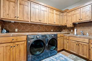 Clothes washing area with a sink, separate washer and dryer, light tile patterned floors, and cabinet space