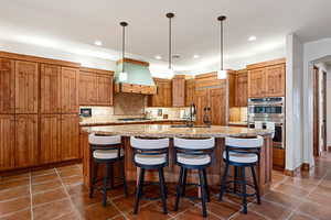 Kitchen with a center island with sink, dark tile patterned flooring, tasteful backsplash, custom range hood, and appliances with stainless steel finishes