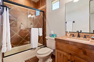 Full bath featuring vanity, bath / shower combo with glass door, and toilet