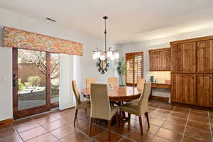Dining room with visible vents, dark tile patterned floors, and a notable chandelier