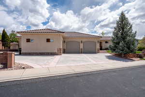 Mediterranean / spanish home with stone siding, stucco siding, a tiled roof, an attached garage, and driveway