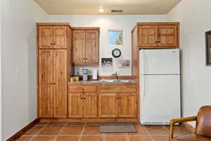 Kitchen with visible vents, brown cabinets, a sink, dark tile patterned flooring, and freestanding refrigerator