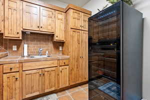 Kitchen featuring light tile patterned flooring, a sink, light countertops, black refrigerator, and decorative backsplash