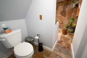 Bathroom with lofted ceiling, baseboards, toilet, and stone tile floors