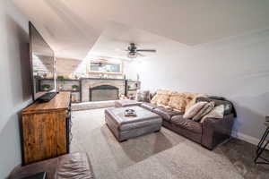 Carpeted living area featuring brick wall, ceiling fan, baseboards, and a fireplace with raised hearth