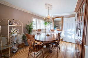 Dining space with crown molding, light wood-style flooring, and an inviting chandelier