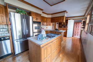 Kitchen with light wood-style floors, tile counters, stainless steel appliances, and ornamental molding