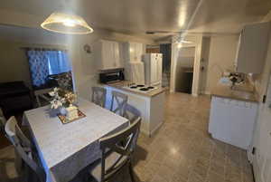 Kitchen with white appliances, tasteful backsplash, a peninsula, white cabinetry, and a sink