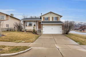 Split level home featuring a porch, a garage, brick siding, driveway, and a front lawn