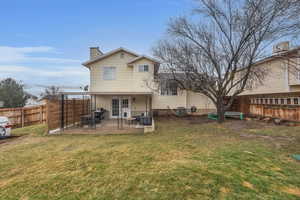 Rear view of house with a patio area, a lawn, a chimney, and a fenced backyard