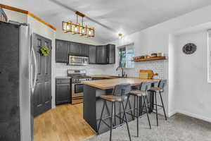 Kitchen featuring lofted ceiling, a peninsula, a sink, wooden counters, and appliances with stainless steel finishes