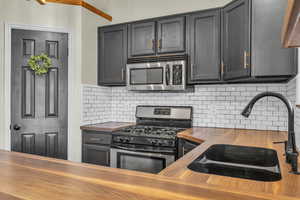 Kitchen with appliances with stainless steel finishes, butcher block countertops, a sink, and decorative backsplash