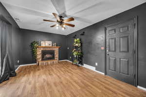 Living room with visible vents, a ceiling fan, a brick fireplace, wood finished floors, and baseboards