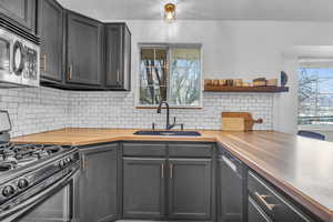 Kitchen featuring dishwashing machine, wood counters, stainless steel microwave, black range with gas stovetop, and a sink