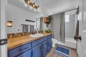 Full bath featuring shower / bath combo with shower curtain, vanity, toilet, and wood finished floors