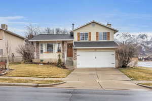 Split level home with a chimney, a porch, a garage, driveway, and a front lawn