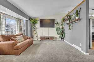 Carpeted living area with vaulted ceiling, visible vents, and baseboards