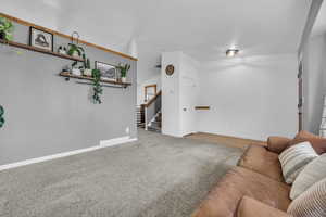 Living room with carpet, visible vents, baseboards, and stairs