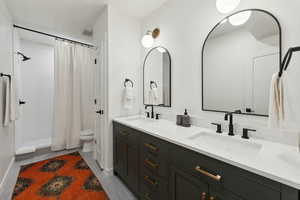 Full bathroom with double vanity, tiled shower, a sink, and toilet