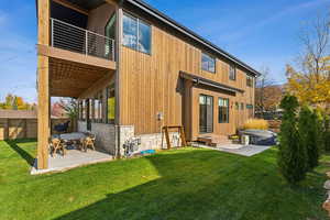 Back of house with a lawn, a patio area, fence, a balcony, and stone siding