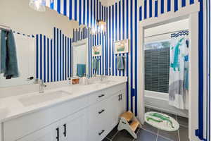 Bathroom featuring double vanity, wallpapered walls, a sink, and tile patterned floors