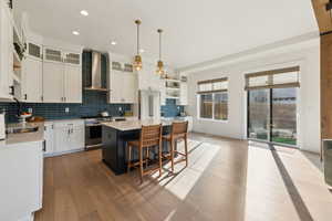 Kitchen with stainless steel appliances, wall chimney exhaust hood, light countertops, and backsplash