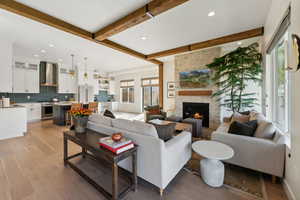 Living area with beam ceiling, recessed lighting, a stone fireplace, wood finished floors, and baseboards