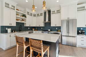 Kitchen featuring open shelves, stainless steel appliances, a sink, wall chimney range hood, and a kitchen breakfast bar