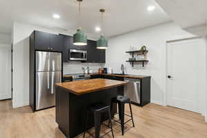 Kitchen featuring light wood-style floors, butcher block counters, stainless steel appliances, and a sink