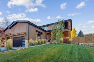 View of front facade featuring a front yard, stone siding, fence, and an attached garage