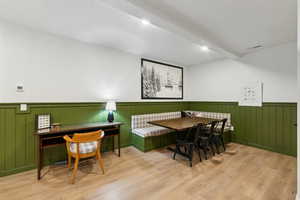 Dining area with a wainscoted wall, breakfast area, beamed ceiling, and wood finished floors