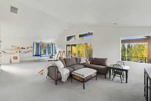 Carpeted living area with high vaulted ceiling, baseboards, and visible vents