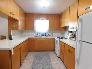 Kitchen featuring tasteful backsplash, white appliances, and light countertops