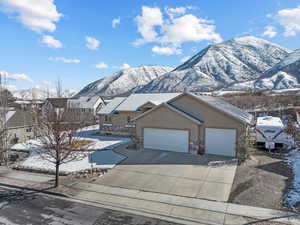 View of front facade featuring stucco siding, a mountain view, a garage, stone siding, and driveway