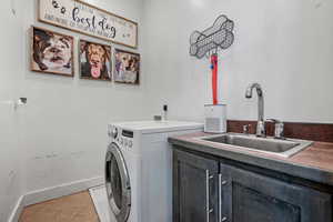Laundry room featuring light tile patterned floors, cabinet space, a sink, washer / dryer, and baseboards