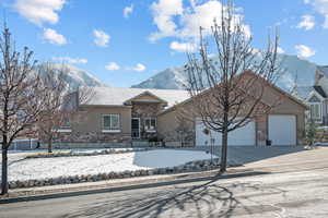 Ranch-style home with stucco siding, an attached garage, a mountain view, stone siding, and driveway